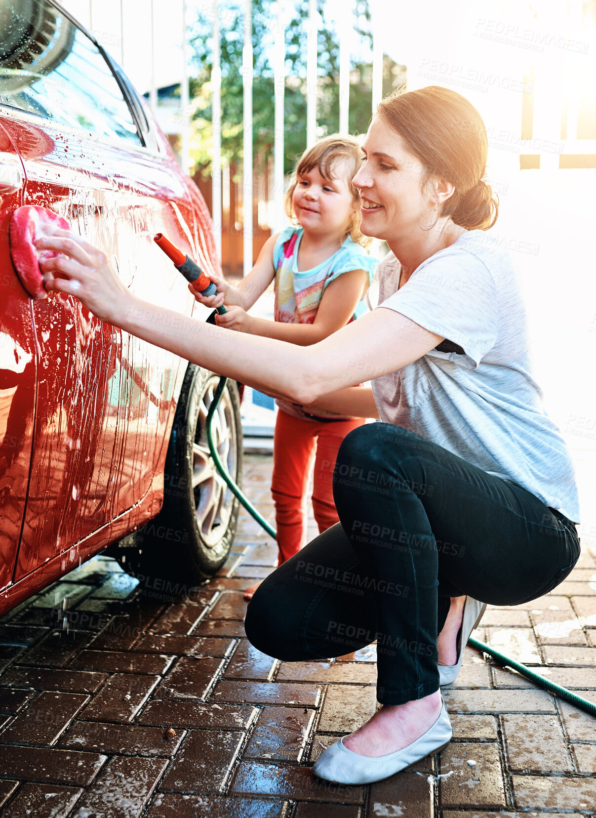 Buy stock photo Love, mother and daughter washing car outdoor for fun, learning or teaching responsibility and bonding. Water splash, hose or woman with kid in driveway for soap foam, cleaning or vehicle maintenance