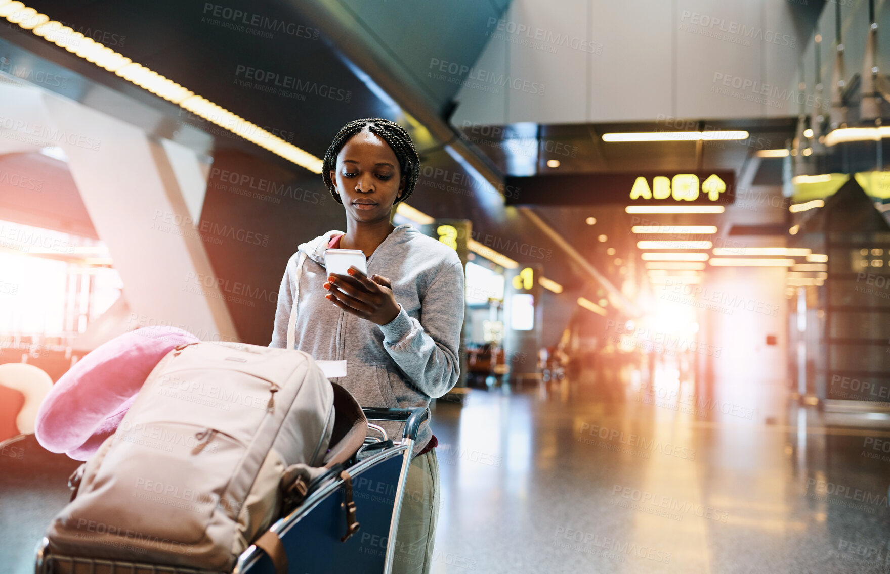 Buy stock photo Woman, airport and luggage with check on phone for travel ticket, reading notification for journey. female person, walking and suitcase in trolley for holiday, mobile app or search for hotel location