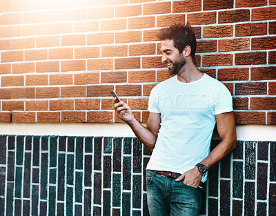 Buy stock photo Casual, man and phone on brick wall for outdoor communication, network and social media chat. Person or online user in Europe with cool fashion, style and tshirt and mobile search for inspiration