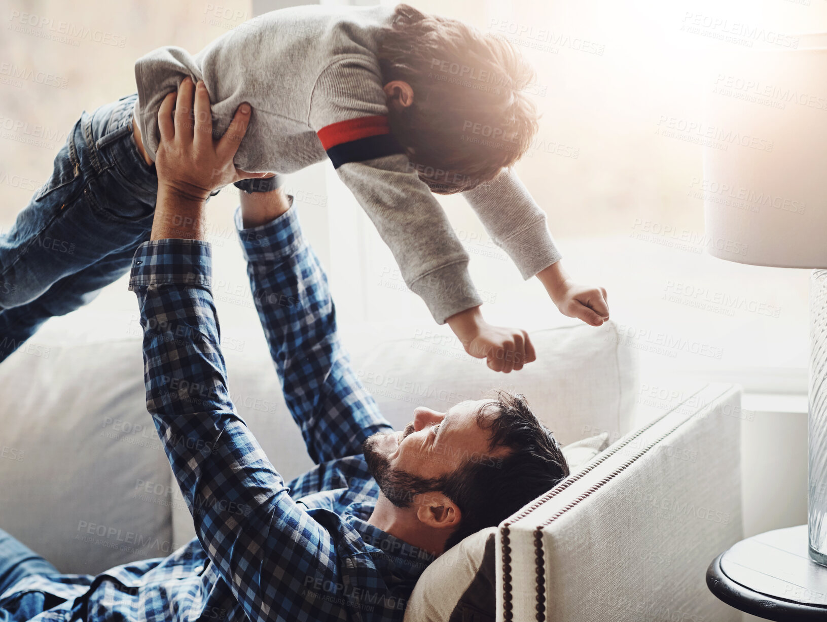 Buy stock photo Relax, boy and father lifting child on sofa for bonding, airplane and playing together in living room. Strong man, lens flare and young kid flying in air for support, game and happiness in home