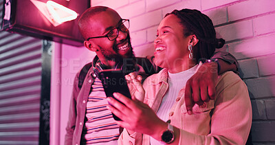 Buy stock photo Black man, woman and together at wall with neon, smartphone and love on night out in city. Fun, couple and laughing with embrace for adventure, enjoyment and excited in urban town with technology