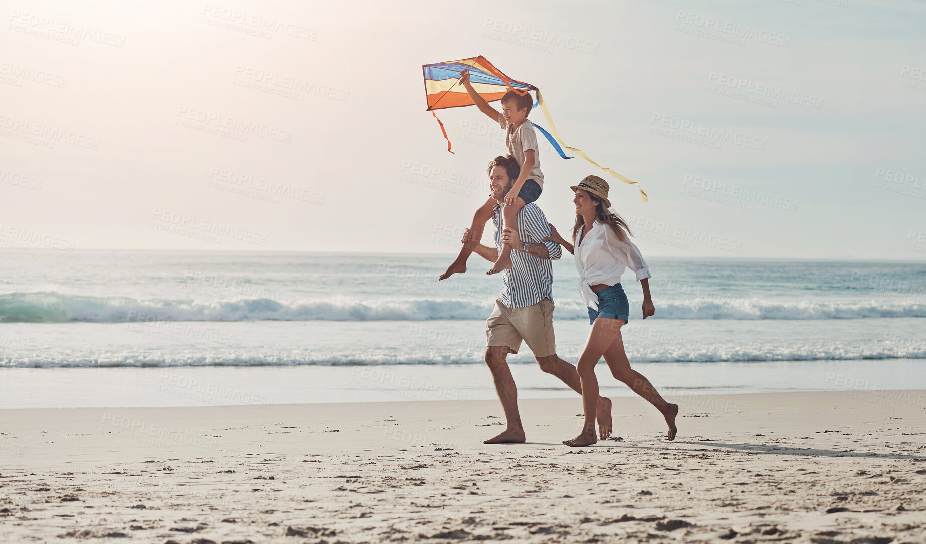 Buy stock photo Family, flying kite and running on beach together for holiday, travel or vacation in summer. Carry, energy or love with mother, father and son on sand at coast by ocean or sea for bonding or freedom