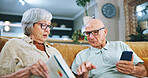 Senior couple, phone and reading with book on sofa for bingo, literature game or dictionary at home. Elderly man or woman checking textbook for online word search or crossword in living room at house