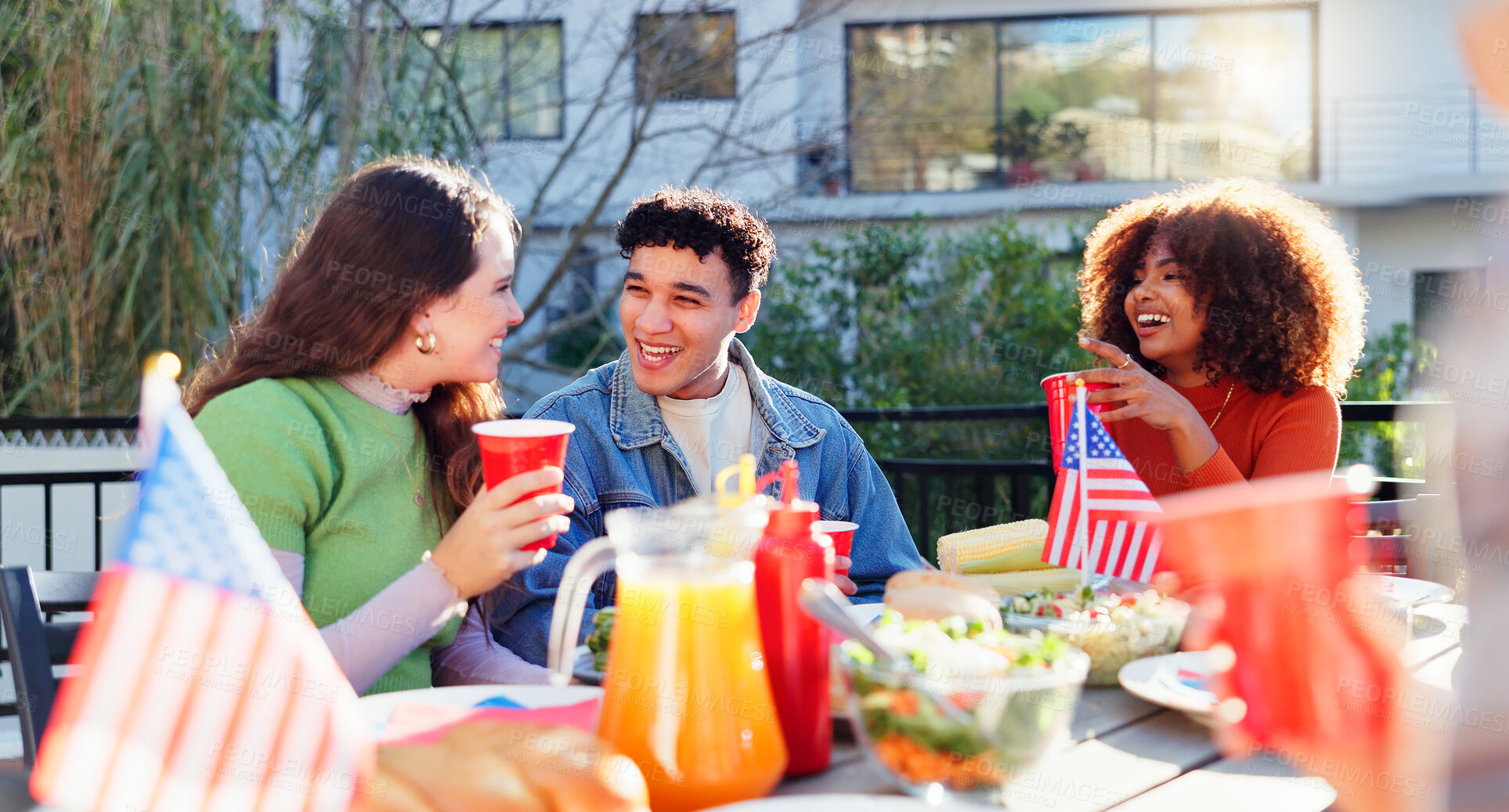 Buy stock photo Friends, celebration and independence day outdoor with food, drinks and talking of international holiday. Social group of people by American Flag, barbecue and lunch at patio table for fourth of July