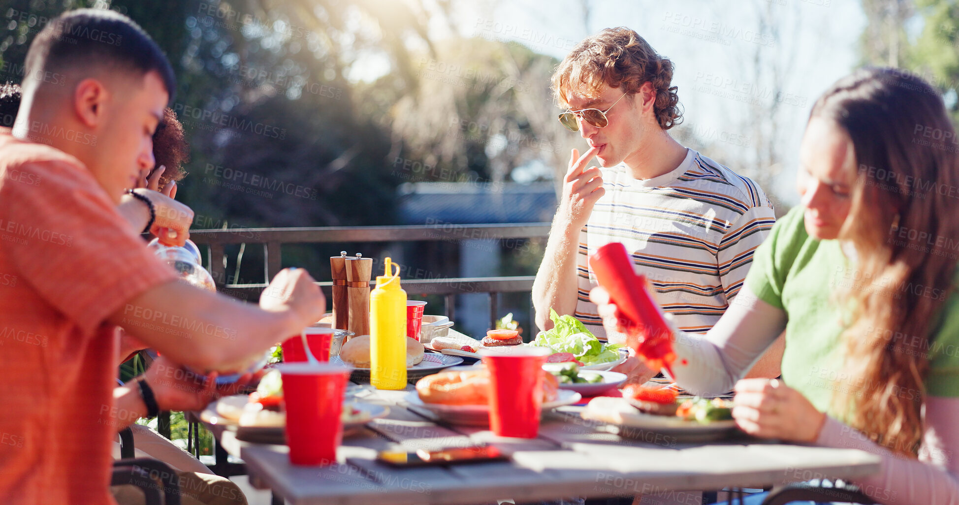 Buy stock photo Friends, group and eating food outdoor on terrace with conversation, reunion or social event in summer. People, barbecue and lunch on patio with bbq, talking and celebration with diversity or drinks