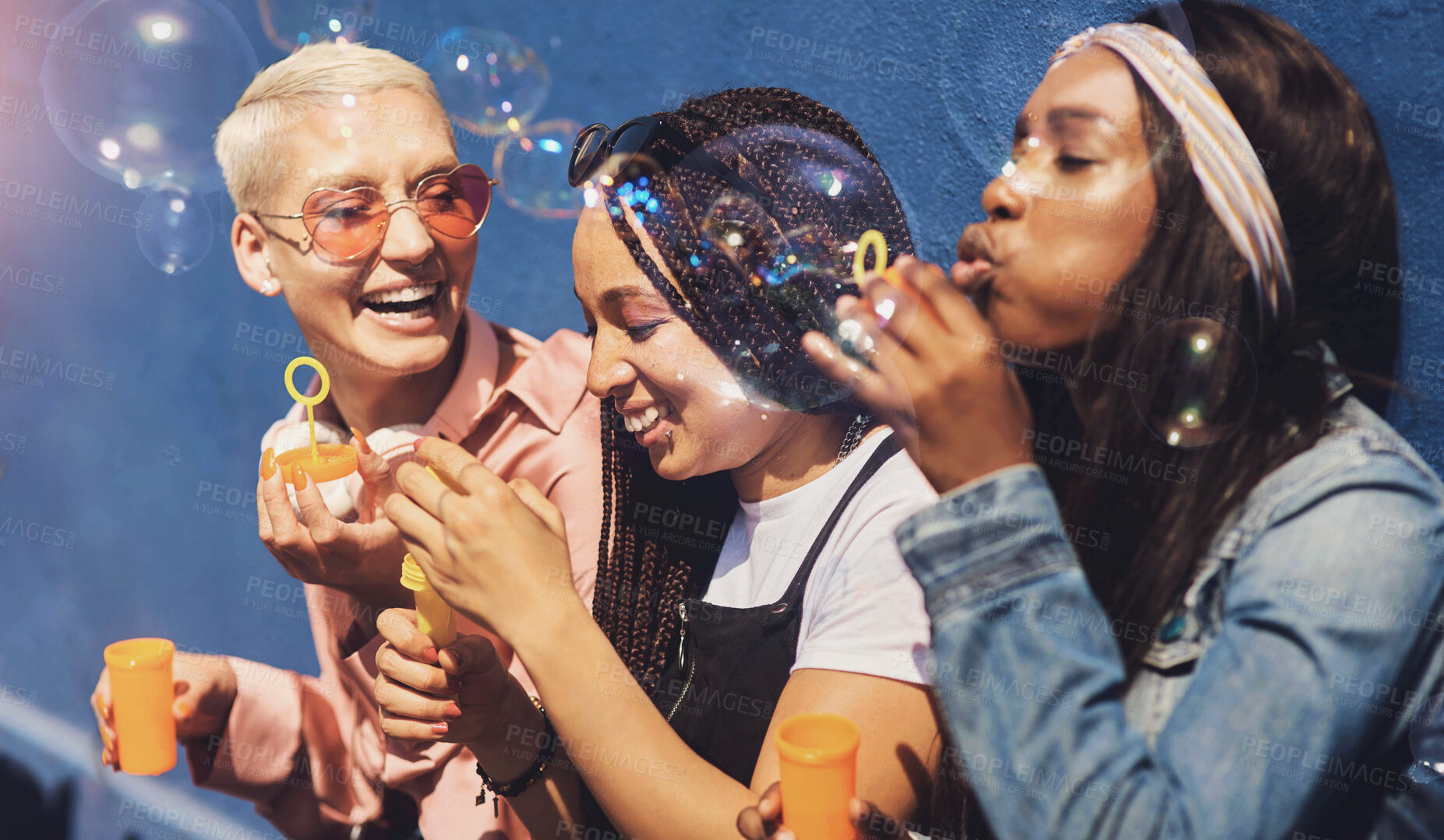 Buy stock photo Women, friends, and blowing bubbles on summer vacation, holiday travel or bonding activity and against a blue wall. Happy, game and ladies playing with soap or wand toy or in freedom and social break