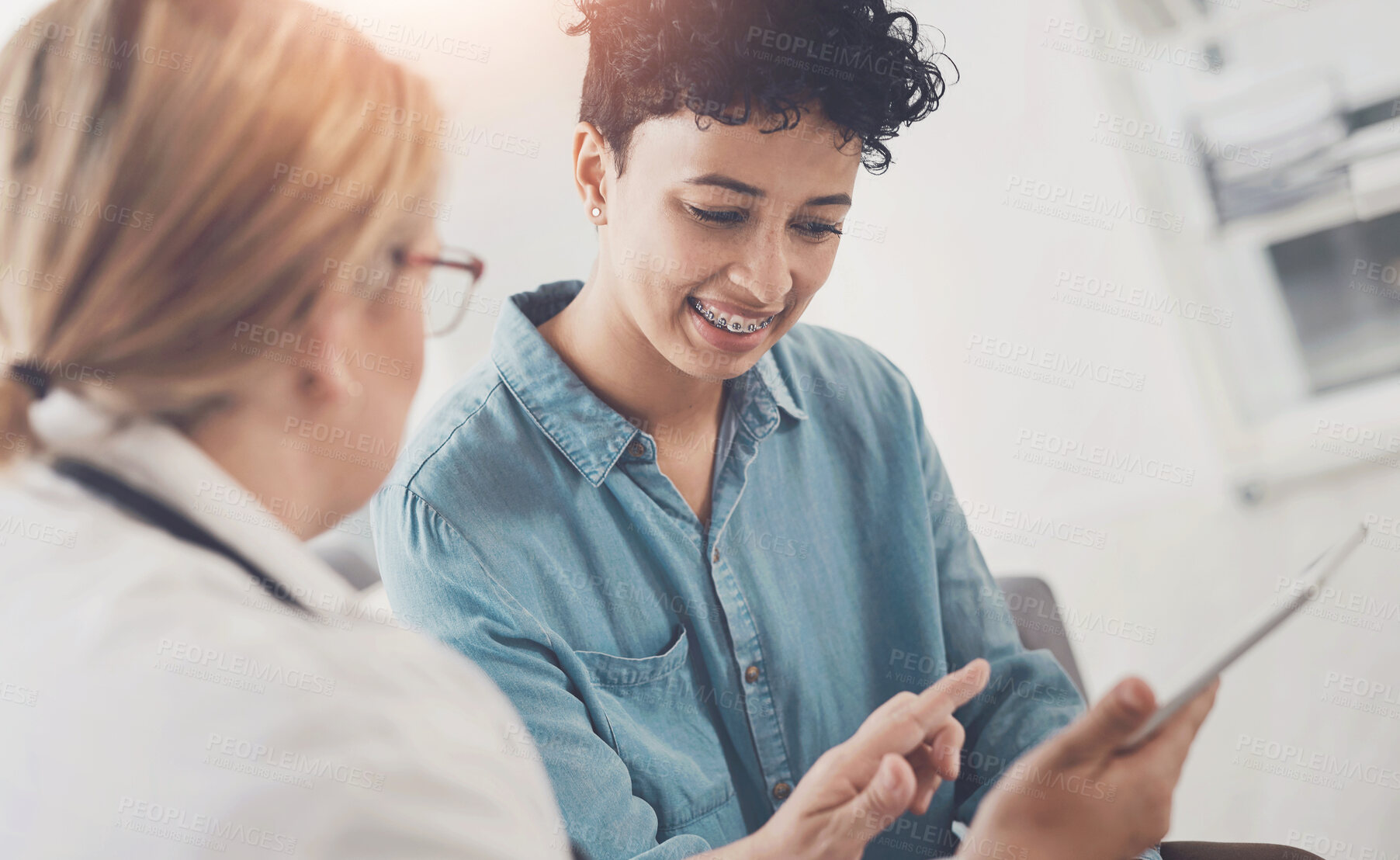 Buy stock photo Cropped shot of an attractive young female doctor using a digital tablet while having a discussion with a female patient in her office
