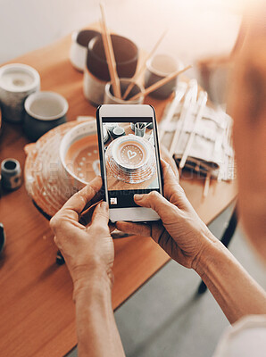 Buy stock photo Cropped shot of an unrecognizable woman standing and taking a picture of her pottery with her cellphone in her workshop