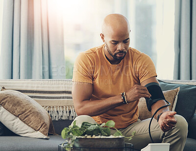 Buy stock photo Shot of a young man taking his blood pressure while sitting on the sofa at home