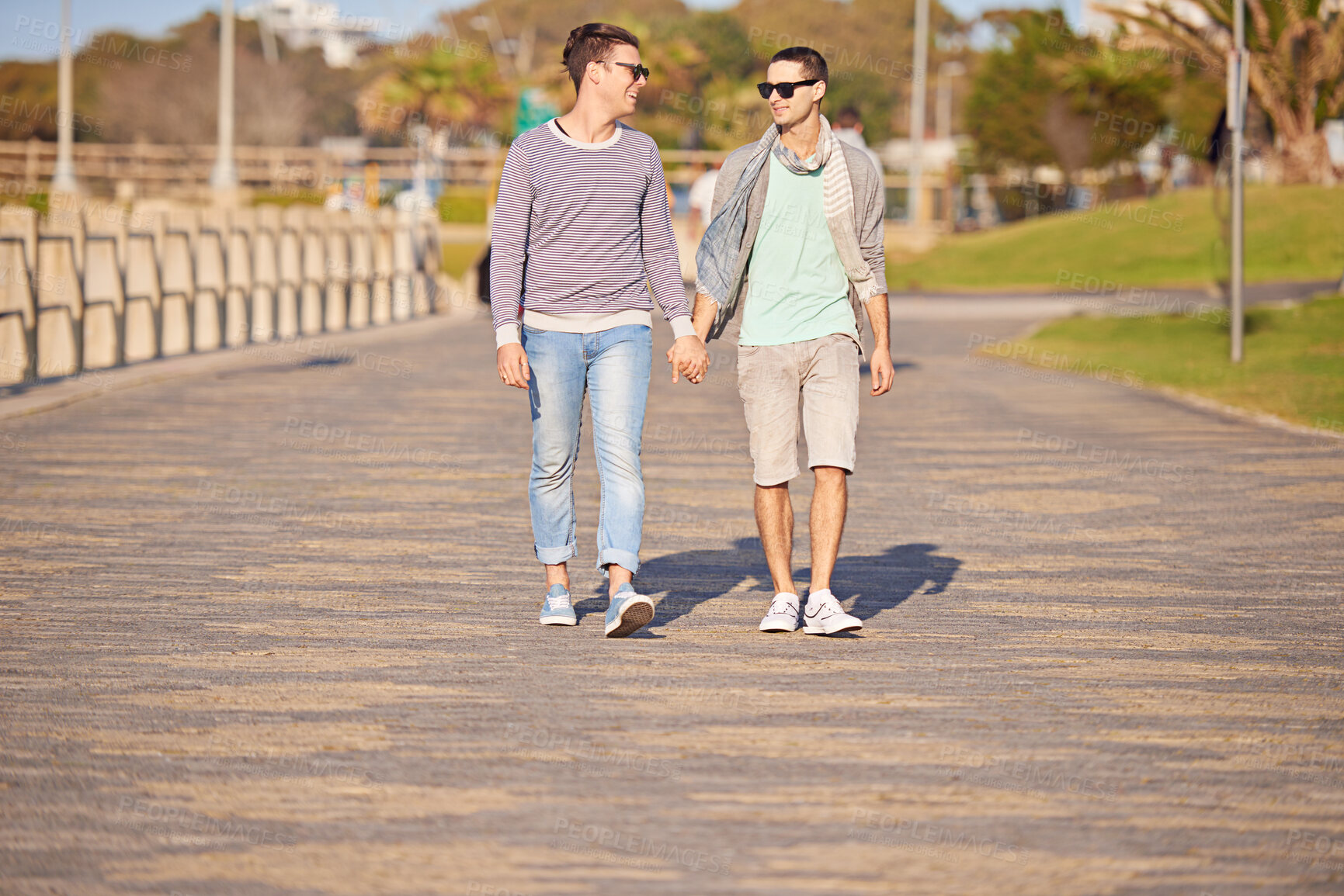 Buy stock photo Holding hands, walking and lgbtq men in park for summer bonding, love and outdoor happiness. Stroll, romance and gay couple on path together for weekend date, relax and partner in sunshine with pride