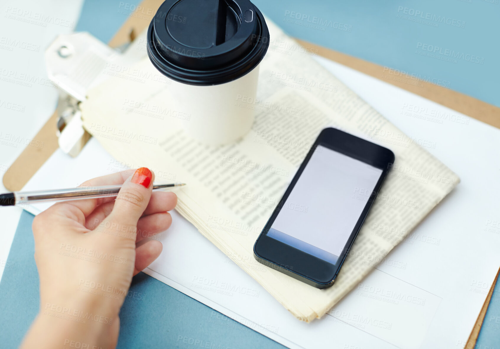 Buy stock photo Disposable cup sitting ontop of a newspaper and clipboard, with a hand holding a pen and a smartphone