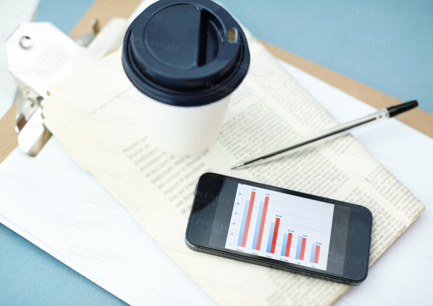 Buy stock photo Smartphone with bar graph on screen sitting ontop of a newspaper and clipboard with a disposable cup and pen