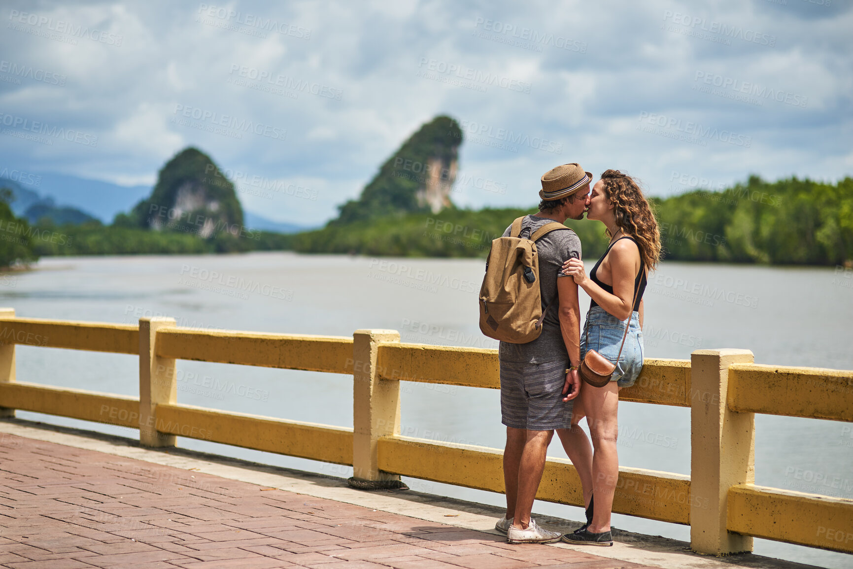 Buy stock photo Travel, couple and happy kiss with vacation, Bali and backpack for adventure by lake. People, together and love on holiday and park path outdoor with support, journey and romance on summer break