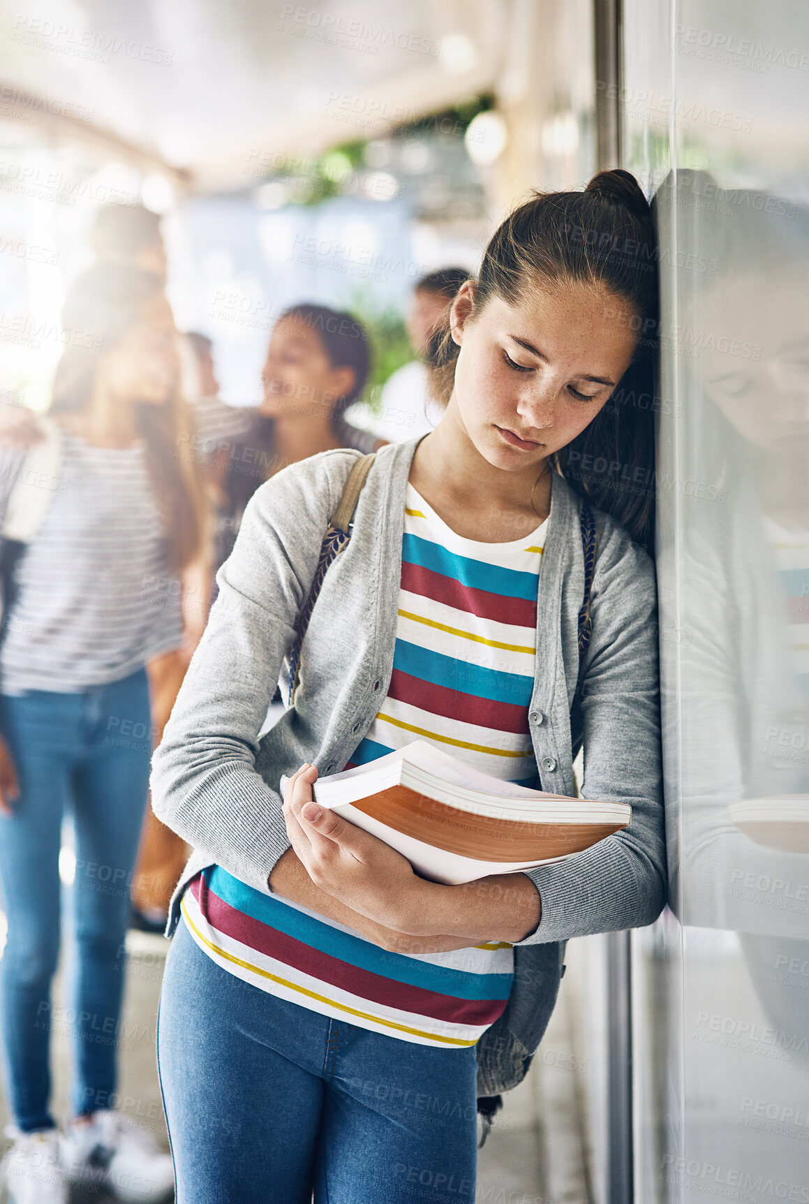 Buy stock photo Shot of a lonely schoolgirl standing outside her classroom with classmates in the background