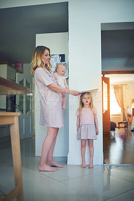 Buy stock photo Shot of a mother carrying her baby and measuring her daughter’s height against a wall