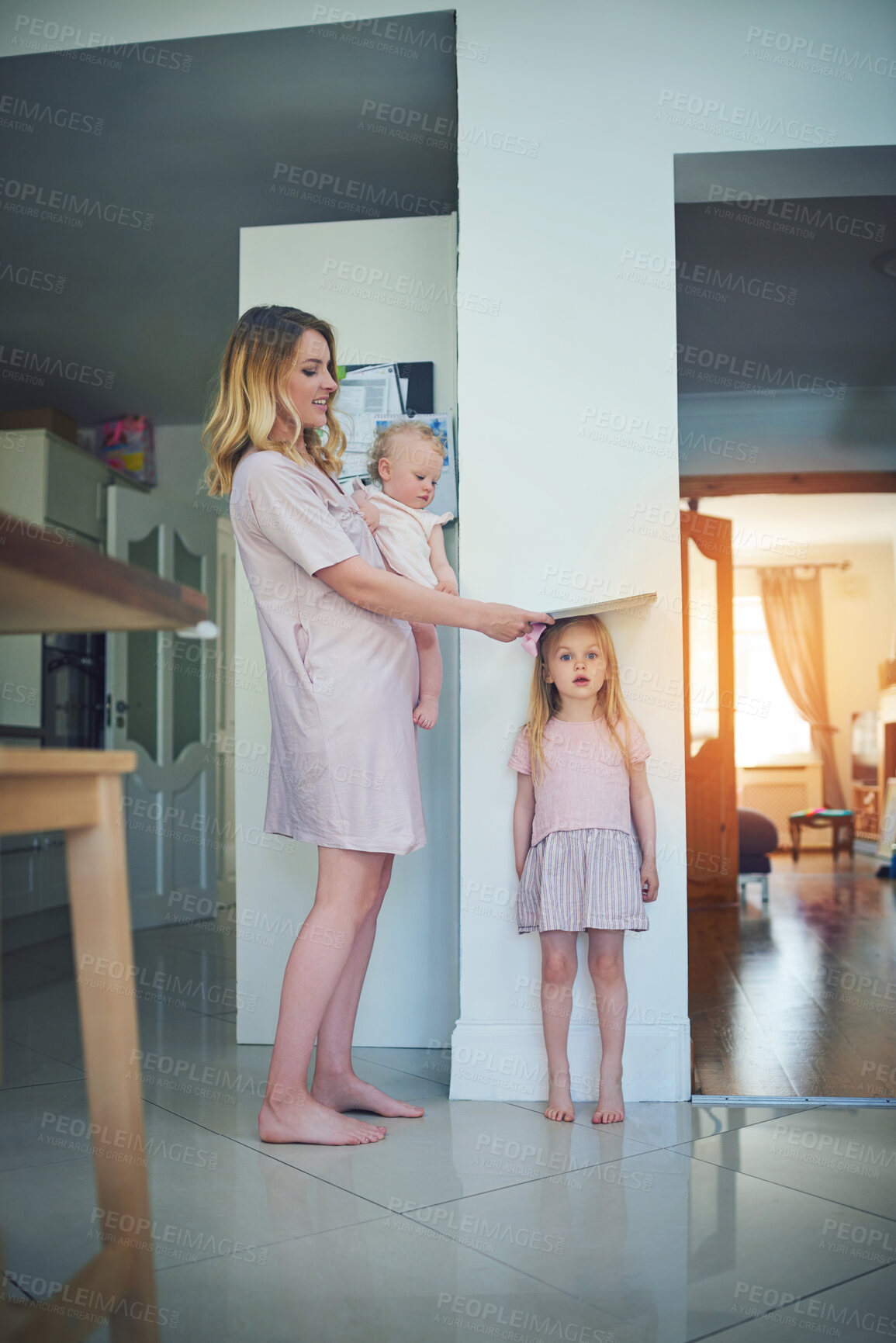 Buy stock photo Shot of a mother carrying her baby and measuring her daughter’s height against a wall