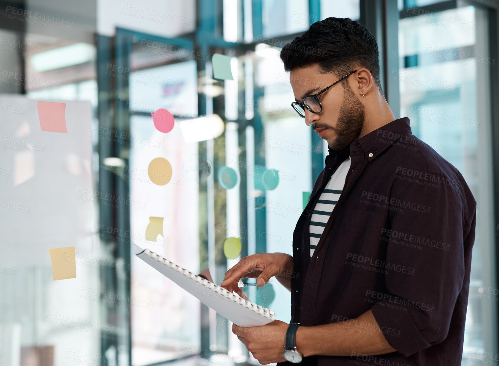 Buy stock photo Business man, reading paperwork or document in office with sticky notes for brainstorming or production plan. Confident, male person or creative director with headshot on transparent wall for casting