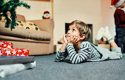 Buy stock photo Christmas tree, gift and boy waiting to celebrate winter holiday, vacation or joyful time in home or house. Kid, development and child lying on carpet, ground or floor to relax in xmas festive season