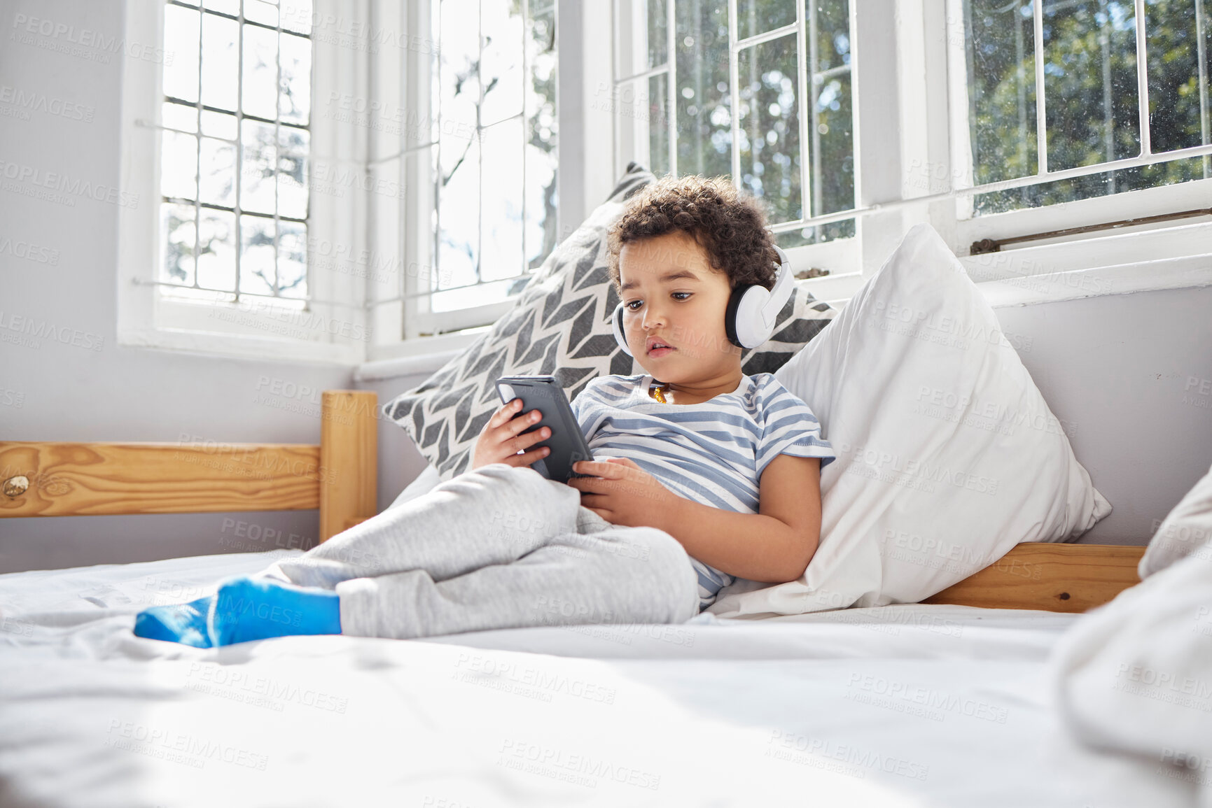 Buy stock photo Bed, phone and boy with headphones for listening, hearing and ebook for learning with children stories. Home, bedroom and kid with mobile app for games, cartoon and streaming videos for curious