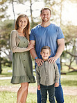 Young happy caucasian family relaxing and standing  together in nature. Loving parents spending time with their little son at the park. Carefree child bonding with mom and dad