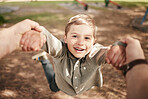 Close up face of happy caucasian boy swinging and spinning in circles by the arms at the park with his father. Cute playful kid having fun while bonding with a parent on a sunny summer outdoors