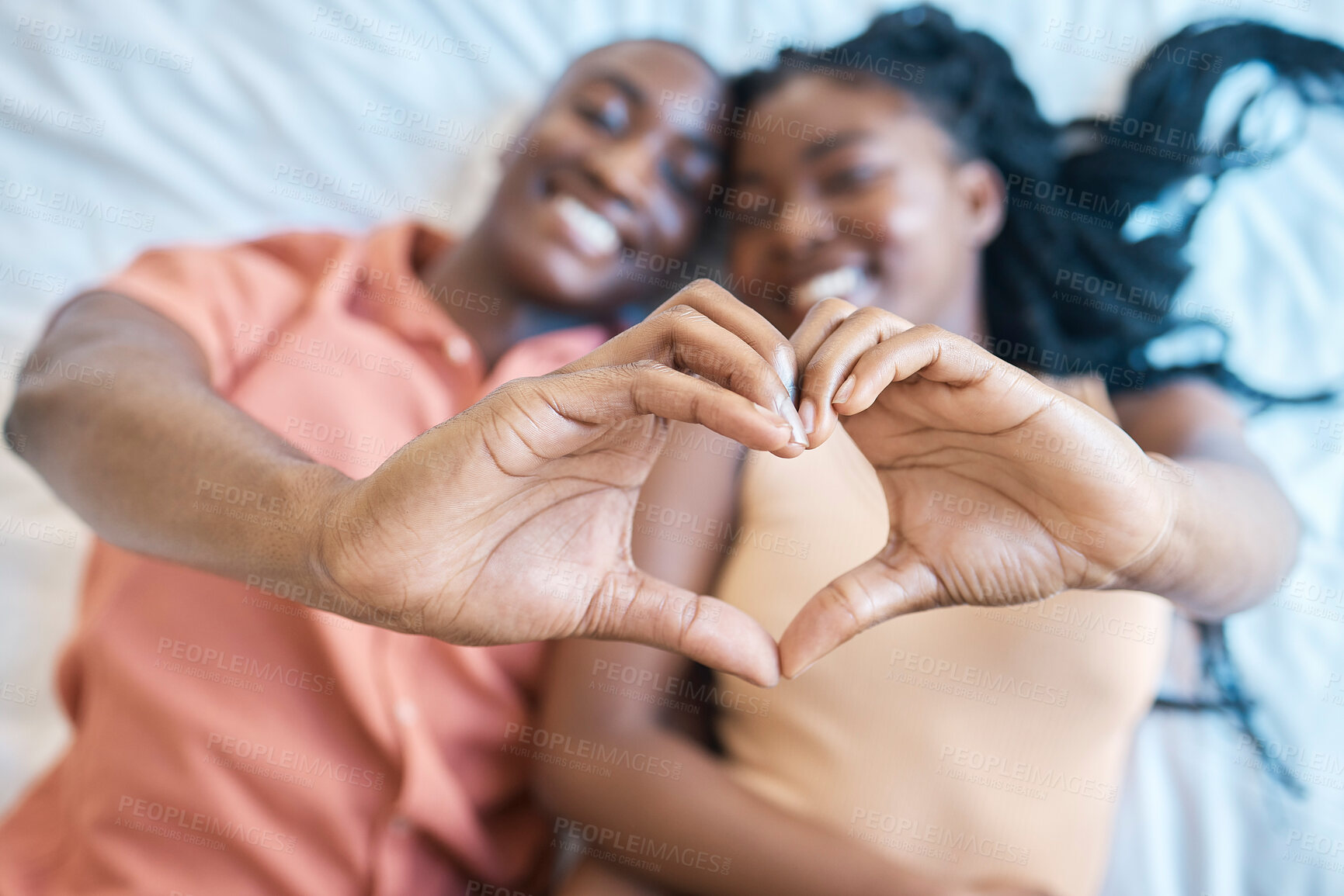 Buy stock photo Black couple, home and happy with hands in heart for bonding together, relationship and commitment. Face smile, African woman and man with love emoji on bed for care, marriage loyalty and kindness