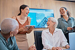 Four happy businesswomen laughing and working together in a boardroom at work. Young cheerful mixed race woman using a digital tablet while doing a presentation in a meeting with coworkers