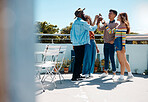 Full length of diverse group of young millennial friends standing outside together and toasting with beers. Smiling men and women being social and celebrating on a rooftop. Weekend party and alcohol