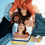 Cheerful group of diverse friends standing in a huddle against a blue sky. Multi-racial millennial friends standing together arms around each other and smiling while looking down at the camera 