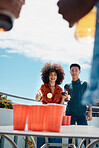 Happy young friends playing beer pong together outside. Diverse friends throwing a ball into cups of beer. Young asian man having fun and playing a game with his hispanic friend.Smiling young friends 