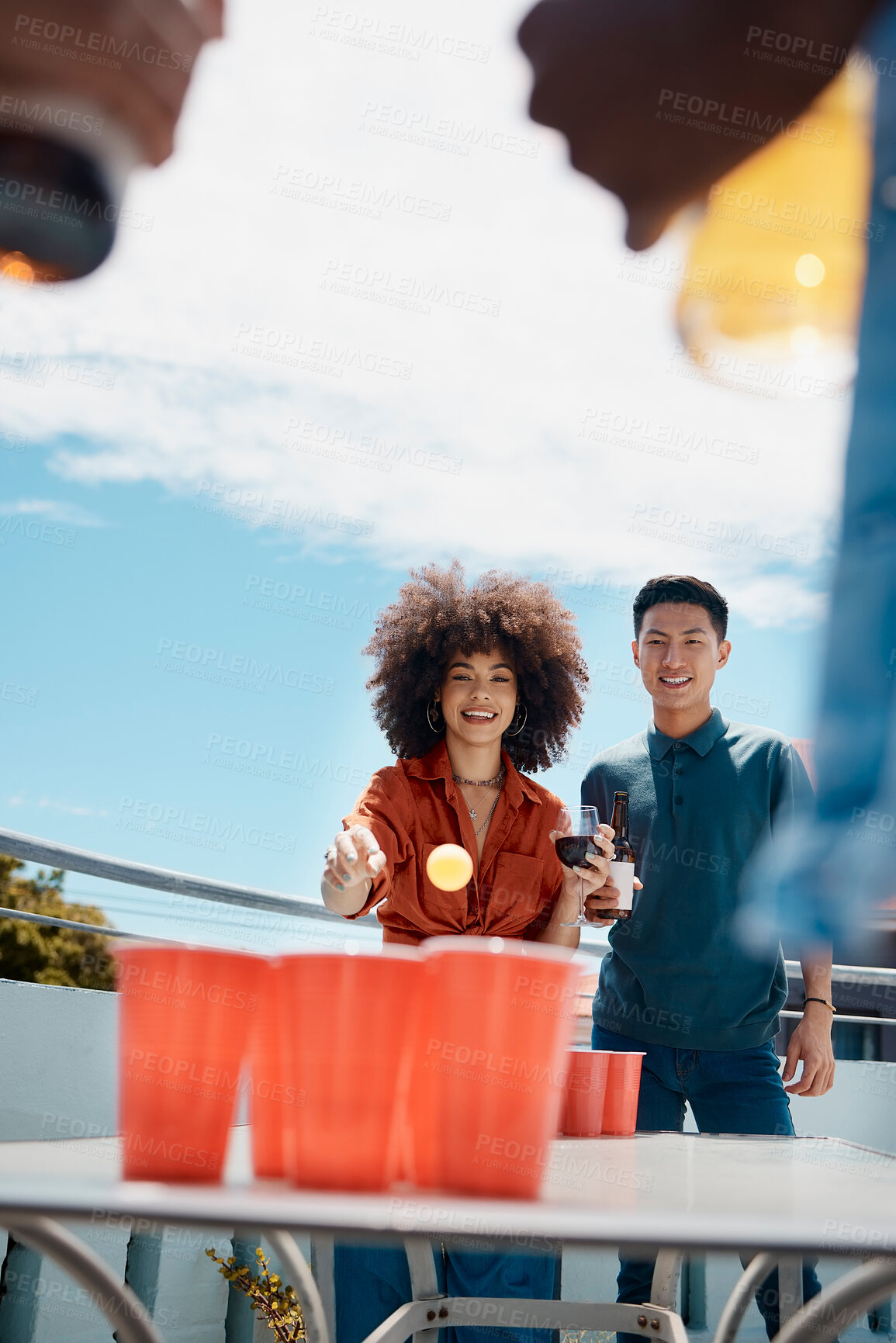 Buy stock photo Happy, friends and play beer pong on rooftop to celebrate Octoberfest. Man, woman and throw ball in cup with alcohol on table at party for competition, game or drink wine with diverse people outdoor