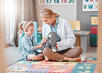 Young caucasian paediatrician helping a little girl listen to the heartbeat of a toy with a stethoscope. Small, happy child visiting the doctor for a checkup, playing on the floor together.