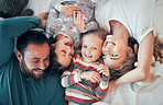 Young caucasian family of four bonding while relaxing in bed together. Young cheerful couple having fun with their two adorable young daughters and taking selfies in bed 