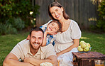 A happy family with a child having a picnic in the garden. Portrait of a smiling, cute little boy with his parents relaxing in the backyard. A mother and father having fun with their son on the grass