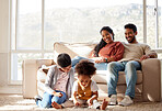 Fullbody of a smiling young mixed race couple sitting close together on the sofa at home and watching their adorable children play. Cute hispanic girls bonding their mother and father in a living room