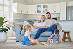 Happy caucasian parents sitting on the couch watching their little son and daughter play with their toys in the lounge at home. Brother and sister playing with their toys together