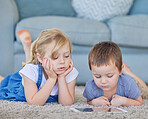 Young caucasian boy and girl watching cartoon videos online and playing fun games on digital tablet to learn from educational apps while lying on the carpet floor at home. Two kids using smart gadget 