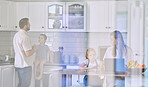 Happy young caucasian family having lunch time with fresh fruit in a bright kitchen. Affectionate father kissing his wife while she's using a laptop and sitting with her kids at home