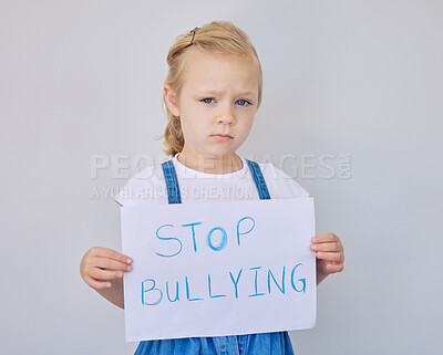 Buy stock photo Paper, portrait and girl with stop bullying sign on studio gray background for victim awareness. Child development, education and sadness with unhappy elementary student holding poster for message