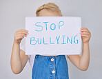 Unhappy and sad little girl holding up a "stop bullying" sign. Adorable little elementary aged girl looking scared while hiding her face and protesting against bullying. Is your child a bully?