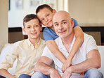 Portrait of happy sons sitting with their father on a comfortable couch at home. Dad bonding with his two kids at home. Mature caucasian man spending time with his children