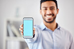 Businessman showing a blank blue screen with copyspace on his cellphone in the office. Mixed race professional holding his phone to display a new webpage and website. Corporate man using technology