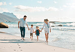 Caucasian family holding hands while enjoying a fun summer vacation at the beach. Loving parents bonding and walking barefoot on the sand shore with their playful carefree little son and daughter