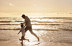 Single dad playing with son on the beach during the day. Caucasian single father bonding with his son and exercising at sunset. Cute little boy enjoying free time with his parent 