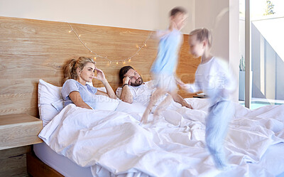 Buy stock photo Parents, bed and headache from jumping children, adhd and chaos in home bedroom on weekend. Excited, energy and siblings with motion blur for speed, tired and overwhelmed man and female person 