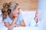 Happy caucasian mother and daughter lying on a bed at home. Cheerful woman with cute little girl enjoying a cosy and lazy relaxing day together. Loving parent bonding and sharing quality time with kid