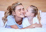 Two blonde caucasian females only looking relaxed and positive while lying in bed together. Young single mother kissing her adorable little daughter on an comfortable bed in a bright bedroom 