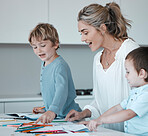 Caucasian mother helping son with homework. Proud mom looking at childs drawings learning about colours. Young mother at home with two sons. Kids using colouring pencils. Teacher tutor with little students