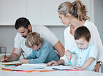 Young caucasian family sitting together at home. Loving parents helping their little children with homework. Carefree siblings focused while writing in notebooks with their mom and dad