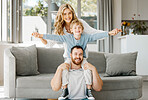 Portrait of playful and excited little boy sitting on his father's shoulders and holding mother's hands while pretending to fly for fun at home. Happy caucasian parents bonding and relaxing with son